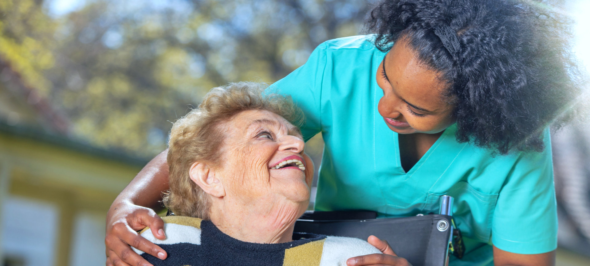 staff and elderly woman on a wheelchair smiling while looking at each other
